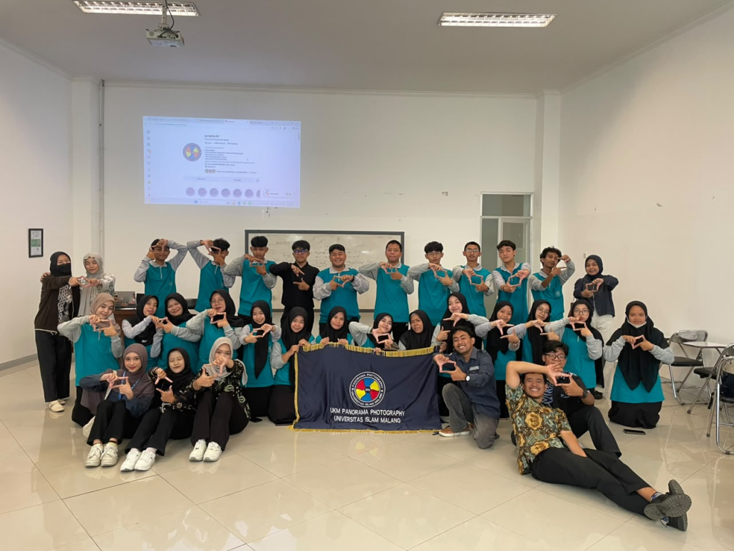 Mahasiswa baru berpose bingkai kamera bersama bendera UKM Panorama Photography pada Master Maba UNISMA 2026 Bidang Keagamaan dan Seni.